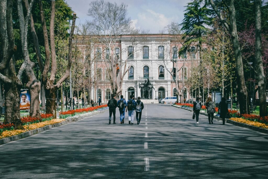 Students walking on a university campus surrounded by trees and spring flowers.